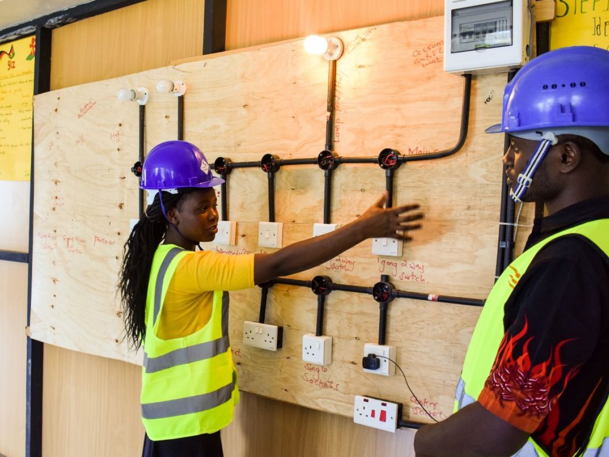 Two young entrepreneurs supported by CAP Youth Empowerment Institute at work, giving a demonstration, in high vis jackets and hard hats